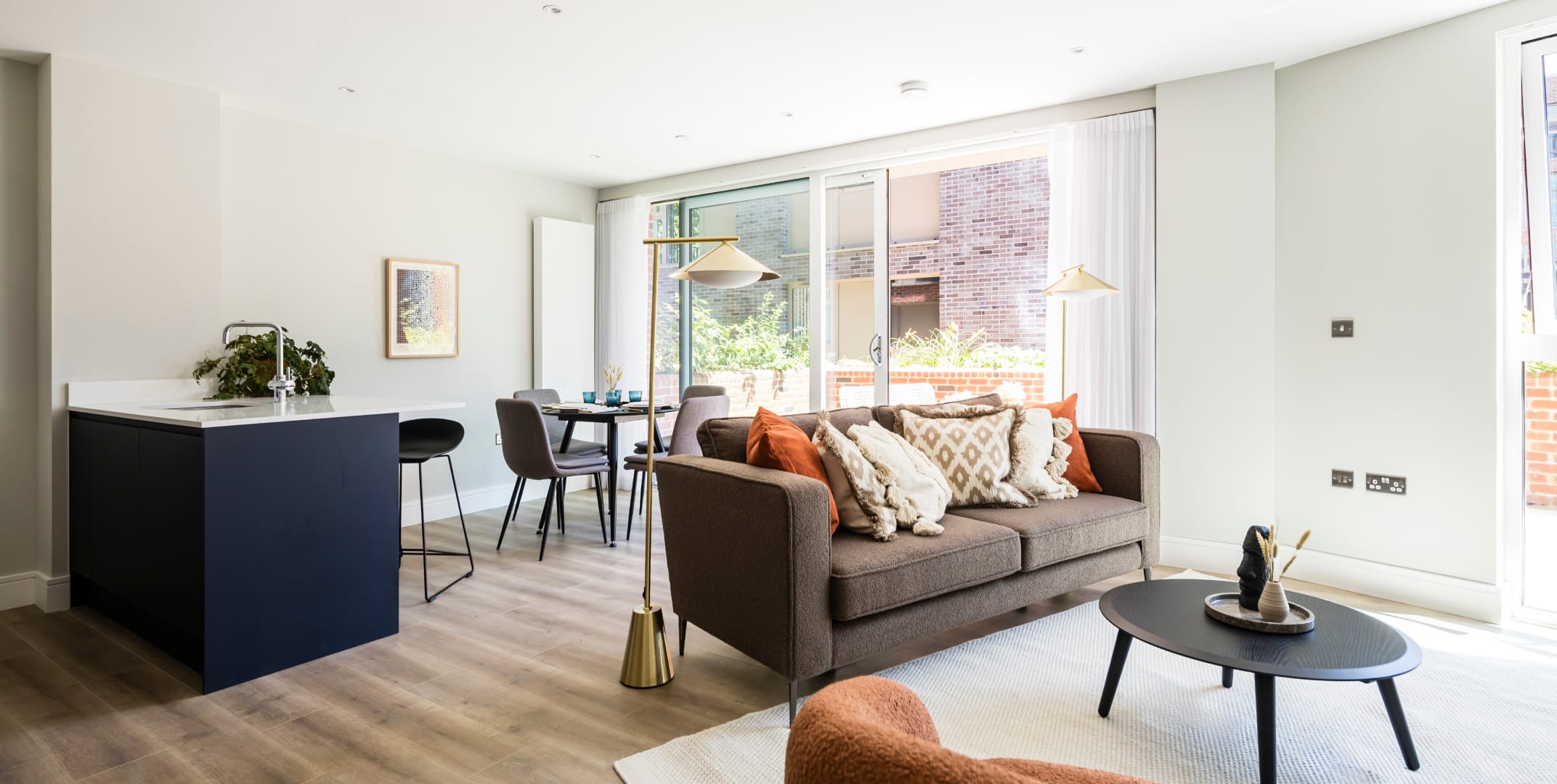 A modern spacious open plan living/dining room with a sofa, armchair, coffee table, dining table and floor lamps. The balcony is visible in the background of the image.