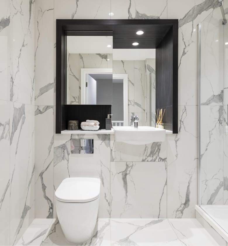 A modern spacious bathroom with white marbled effect tiles and chrome fittings.