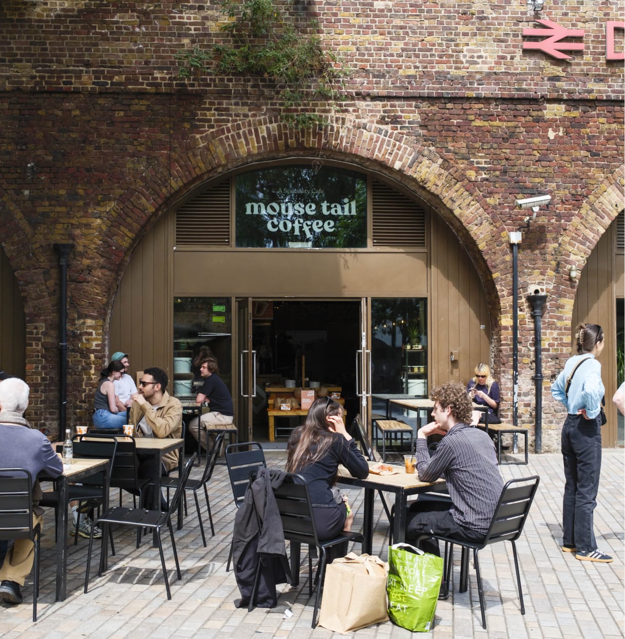 An outdoor shot of the entrance to Mouse Tail Coffee in Deptford. There are many people using the outdoor seating.