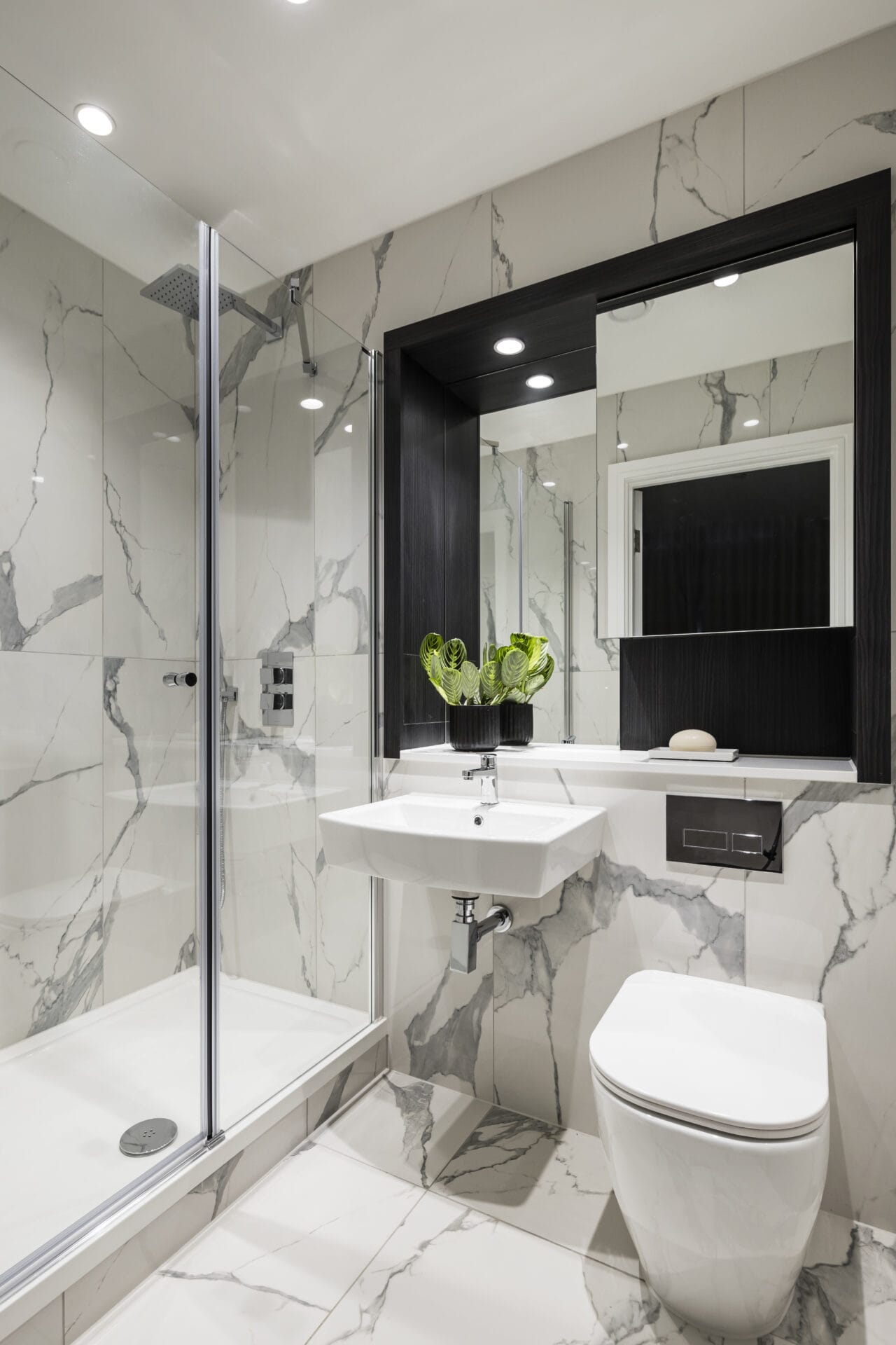 A modern spacious bathroom with white marbled effect tiles. There is a walk-in shower and chrome fittings.