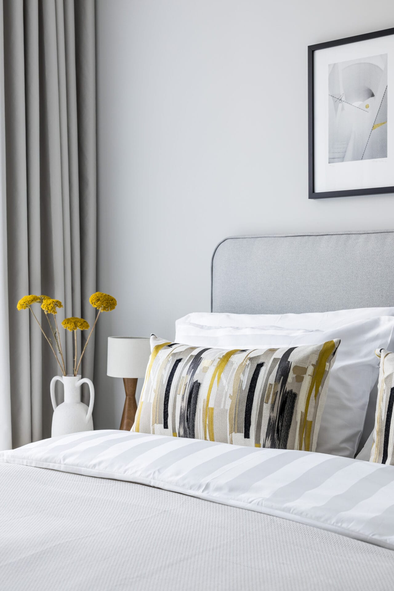 A close up shot of the king size bed with decorative pillows. There is a lamp and vase of flowers on the bedside table.