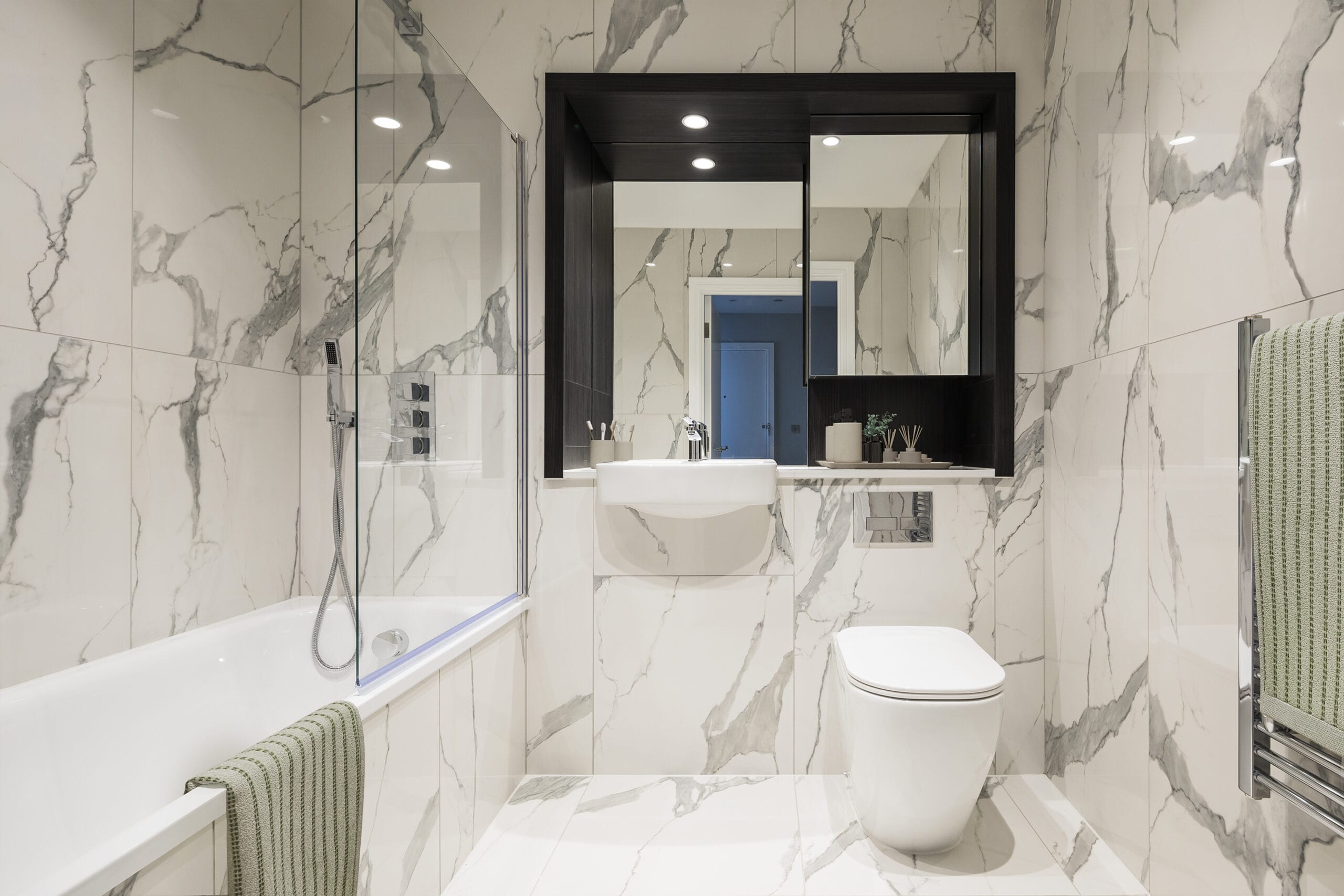 A modern spacious bathroom with white marbled effect tiles. There is a bath and chrome fittings.