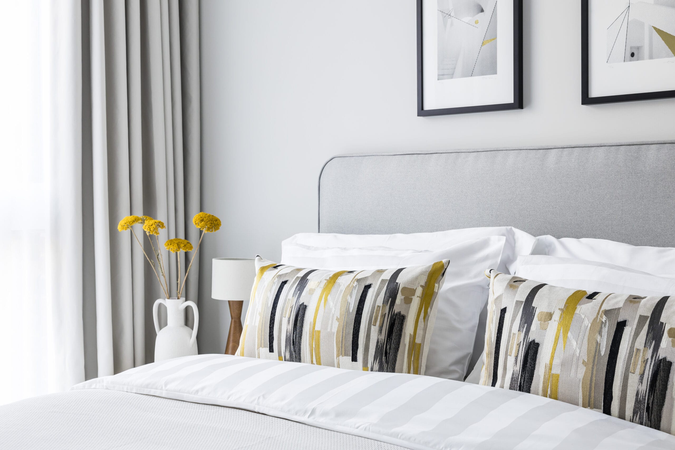 A close up shot of the king size bed with decorative pillows. There is a lamp and vase of flowers on the bedside table.