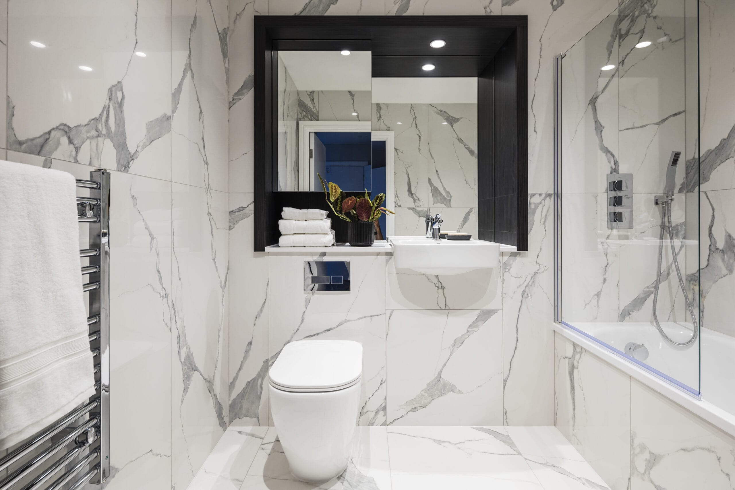 A modern spacious bathroom with white marbled effect tiles. There is a bath and chrome fittings.
