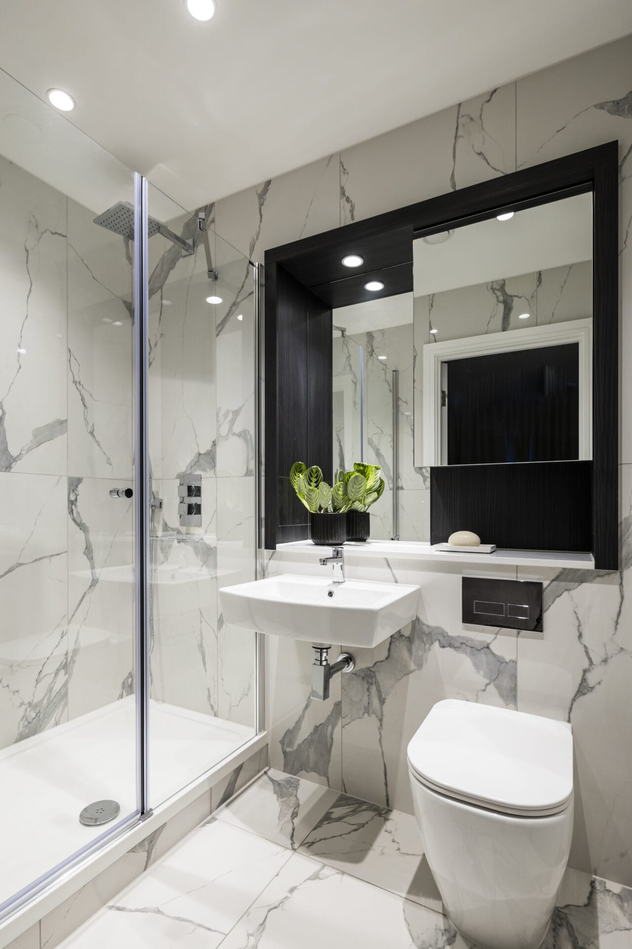 A modern spacious bathroom with white marbled effect tiles. There is a walk-in shower and chrome fittings.