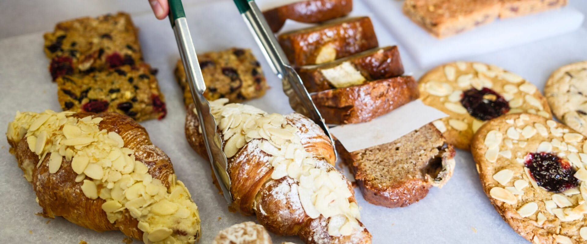 Cafe staff serving a fresh pastry with tongs.