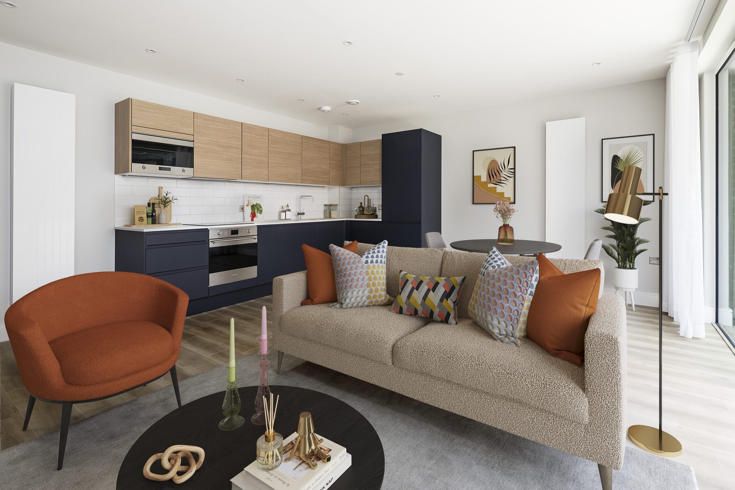 A modern spacious open plan living/dining room with a sofa, armchair, coffee table, dining table and a floor lamp. The kitchen with integrated appliances is visible in the background of the image.