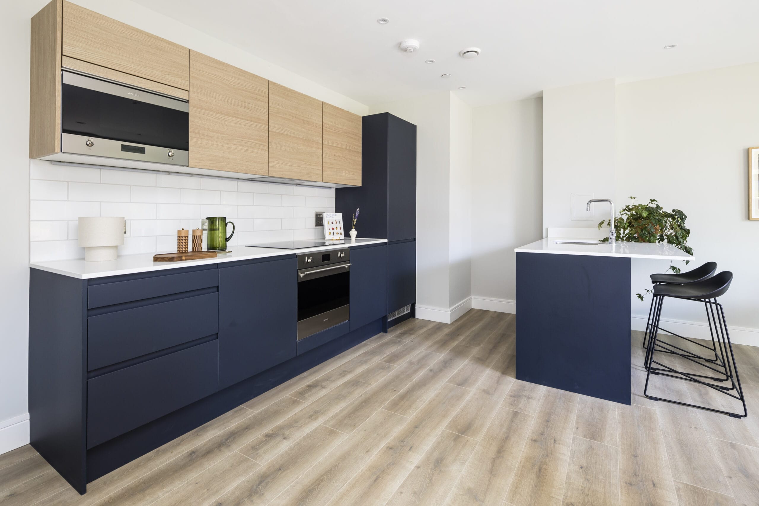 A modern kitchen with a kitchen island/breakfast bar and integrated appliances. The lower cupboards are a dark blue and the upper cupboards are a light wood.
