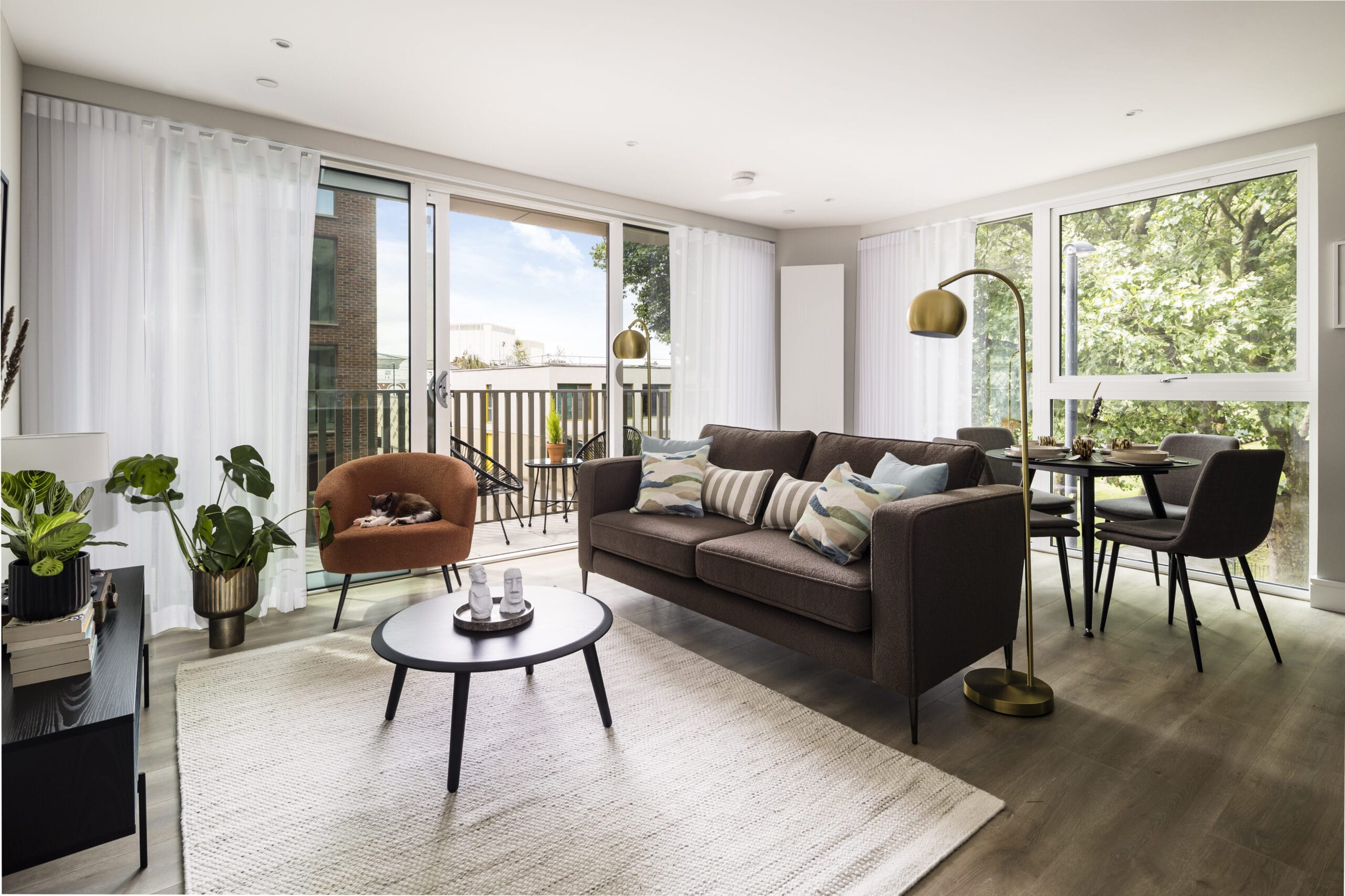 A modern spacious open plan living/dining room with a sofa, armchair, coffee table, dining table and floor lamps. The balcony is visible in the background of the image.