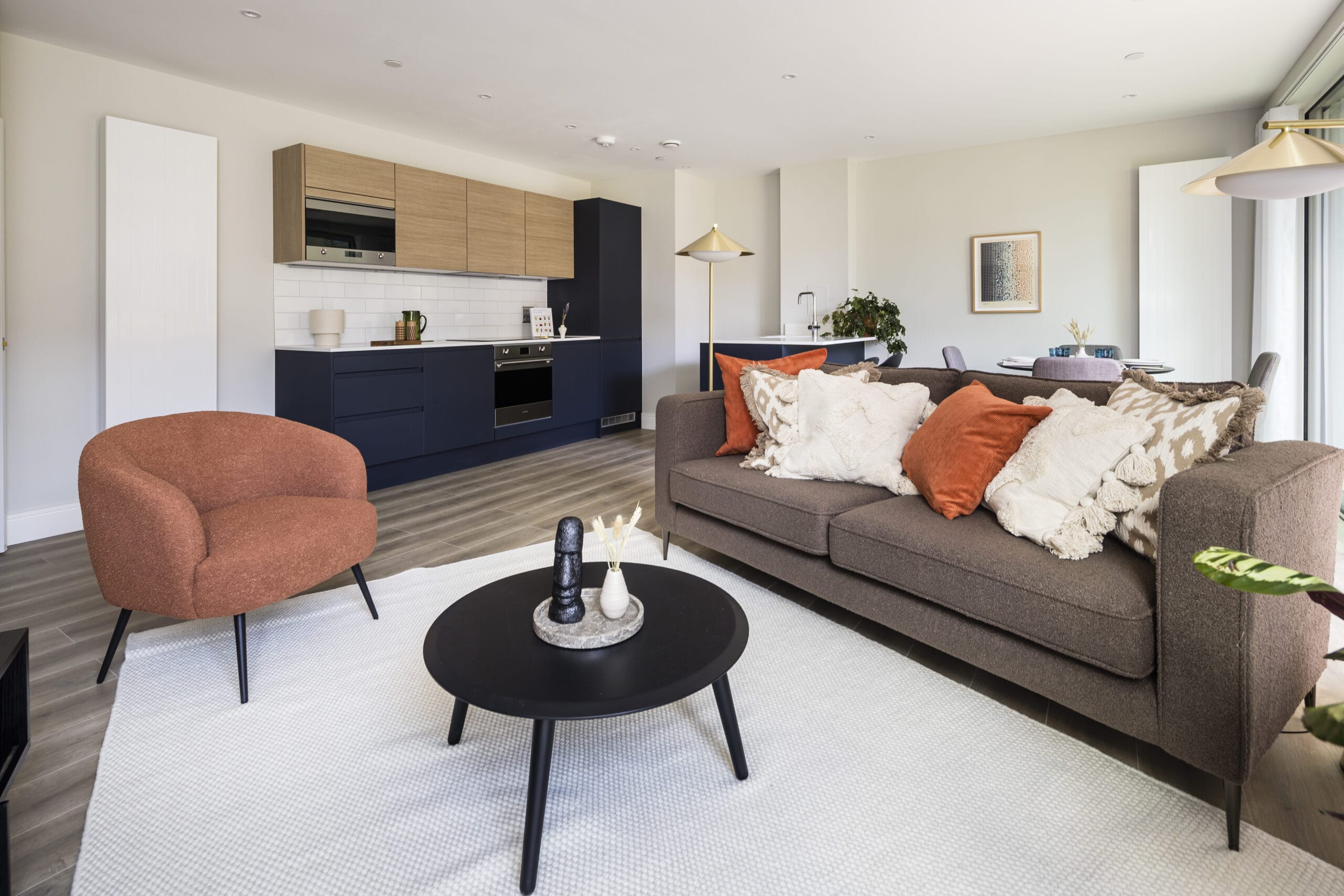 A modern spacious open plan living/dining room with a sofa, armchair, coffee table, dining table and floor lamps. The kitchen is visible in the background of the image.