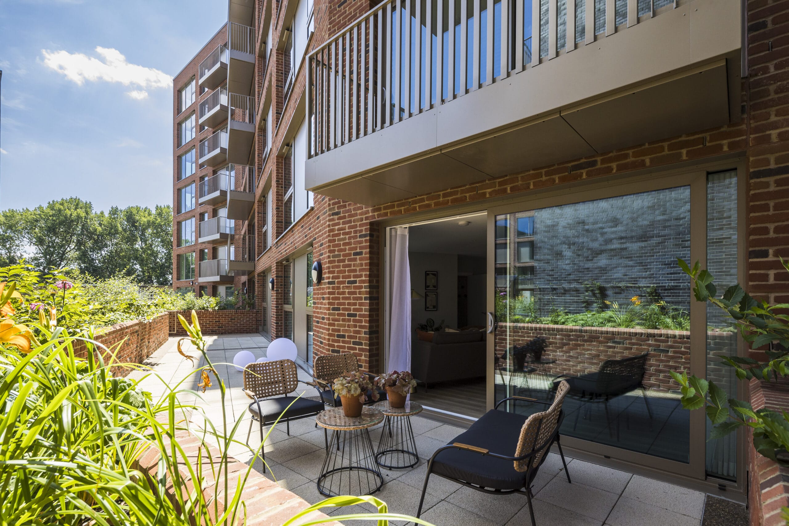 A private outdoor terrace overlooking Deptford Park. The terrace spans the entire length of the apartment unit and features lounge furniture such as rattan chairs and coffee tables.