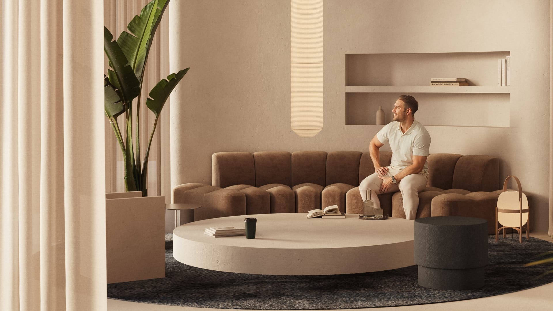 Man sitting on a sofa in the residents lounge, there is a large plant, decorative lamps and a large coffee table.
