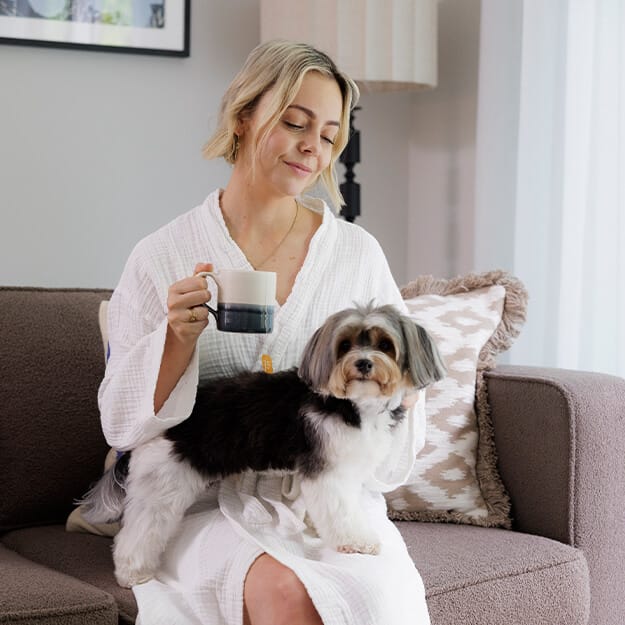 A lady sitting on her sofa with a dog.