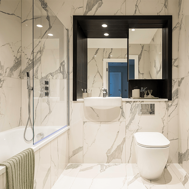 A modern spacious bathroom with white marbled effect tiles. There is a bath and chrome fittings.
