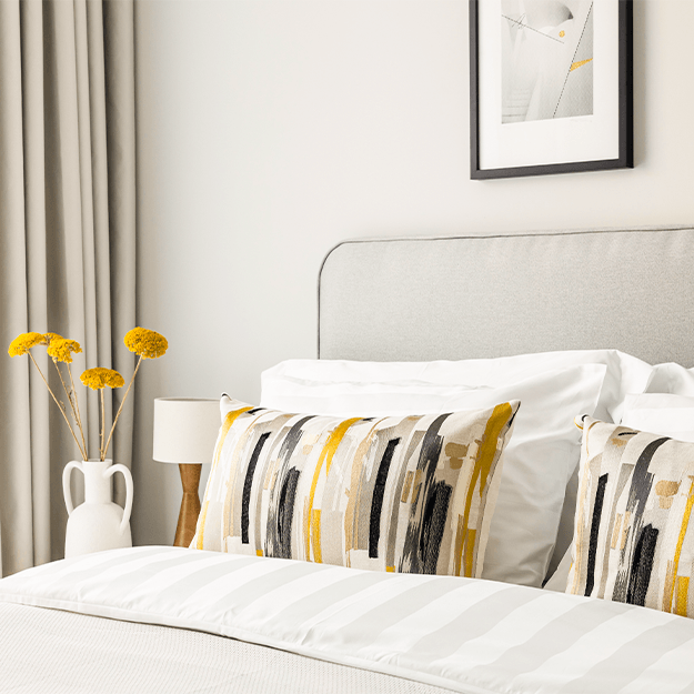 A close up shot of the king size bed with decorative pillows. There is a lamp and vase of flowers on the bedside table.