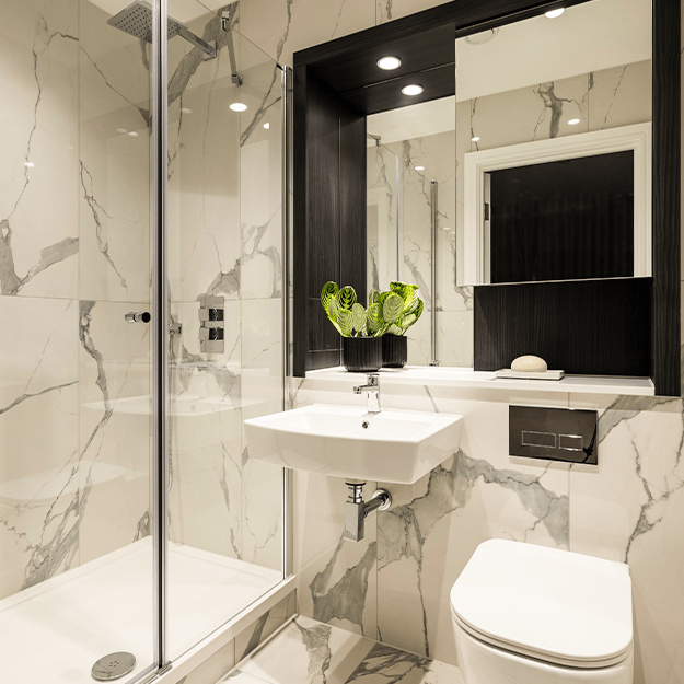 A modern spacious bathroom with white marbled effect tiles. There is a walk-in shower and chrome fittings.